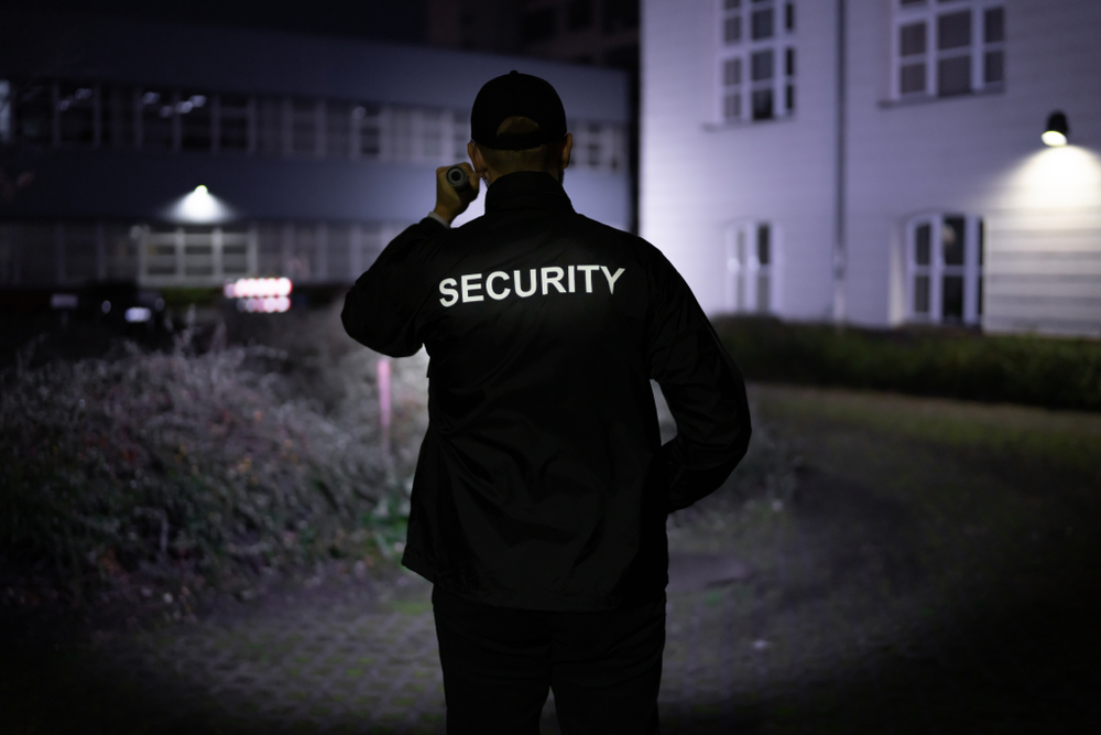 Security,Guard,Walking,Building,Perimeter,With,Flashlight,At,Night Security Guard Walking around a building at night